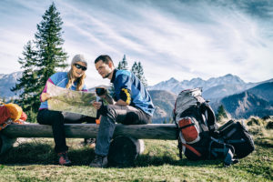 Man and woman hikers hiking in mountains. Young couple camping looking at map and planning trip or get lost. Getting rest and drinking coffee or tea